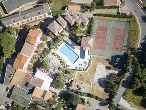 An aerial view of a residential area with a swimming pool, tennis courts, and multiple houses with tiled roofs. - Hôtel Maristella (Aregno)