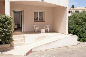 Un edificio con un área de estar al aire libre cubierta, una escalera que conduce a la entrada y una puerta.