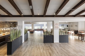 A spacious indoor area with wooden flooring, black planters with plants, and multiple dining tables and chairs. - Hôtel Maristella (Aregno)