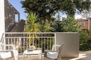 A balcony with white chairs, a small table, and a potted plant.