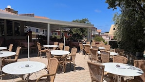 An outdoor seating area with wicker tables and chairs, a covered patio, and a view of buildings in the background. - La Residence Maristella (Aregno)