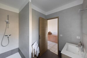 Un baño moderno con ducha, bañera y una puerta de madera que da a un balcón.