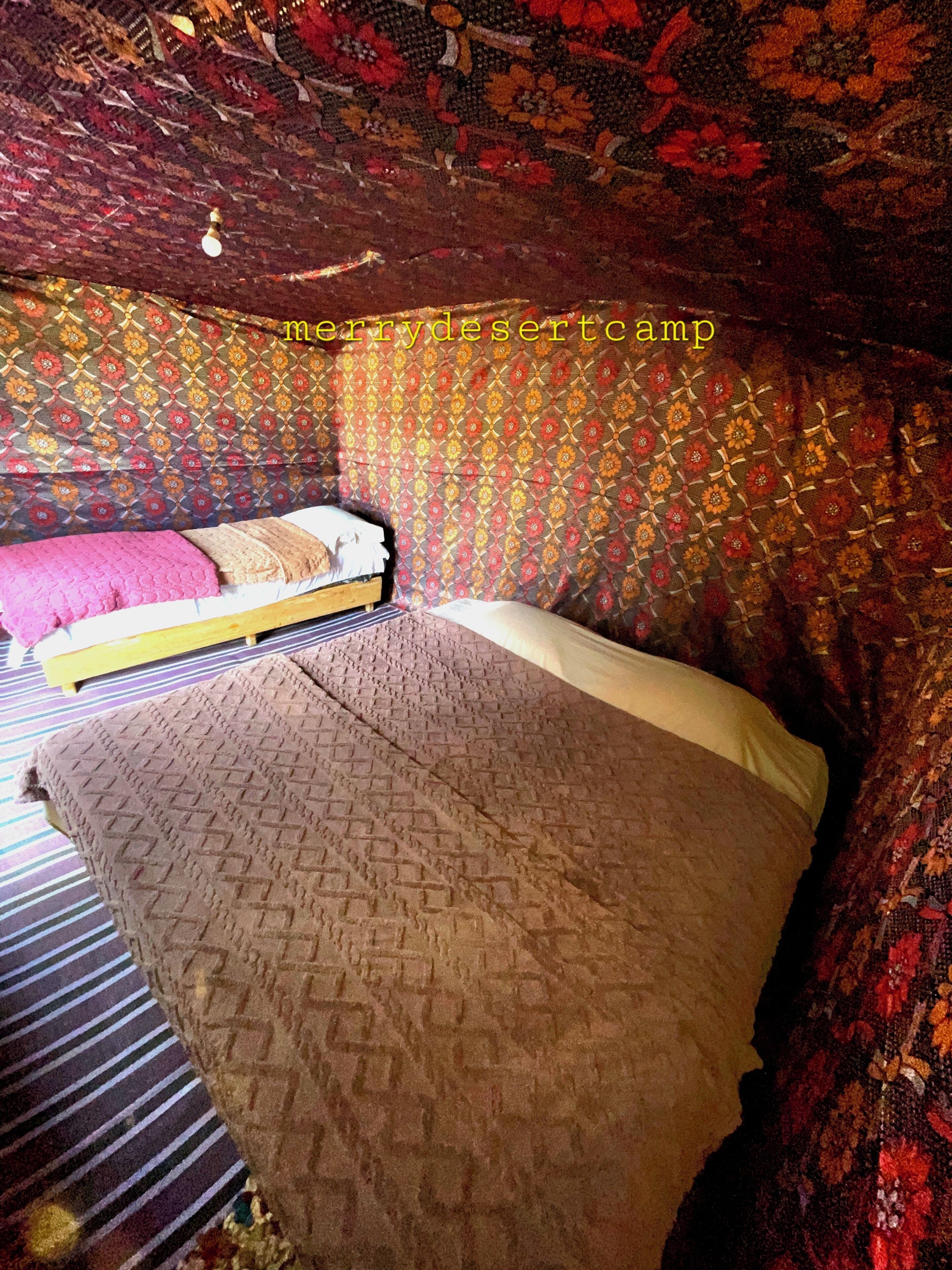Ein Bett mit einem gemusterten Überwurf und Kissen, einem Streifenmuster-Teppich und einer Wand mit Muster.