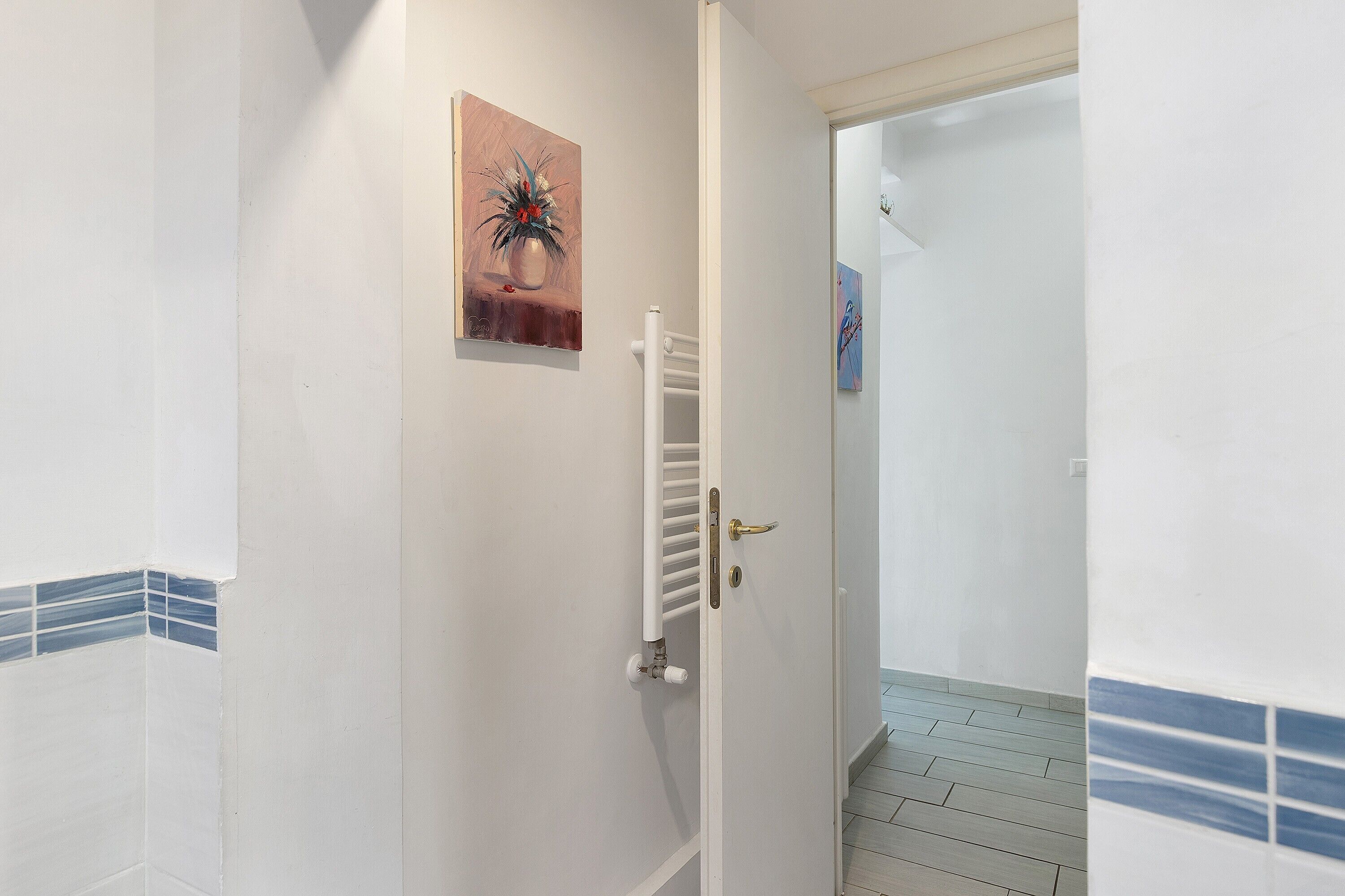 A hallway with a white radiator, a door with a gold handle, and a tiled floor.