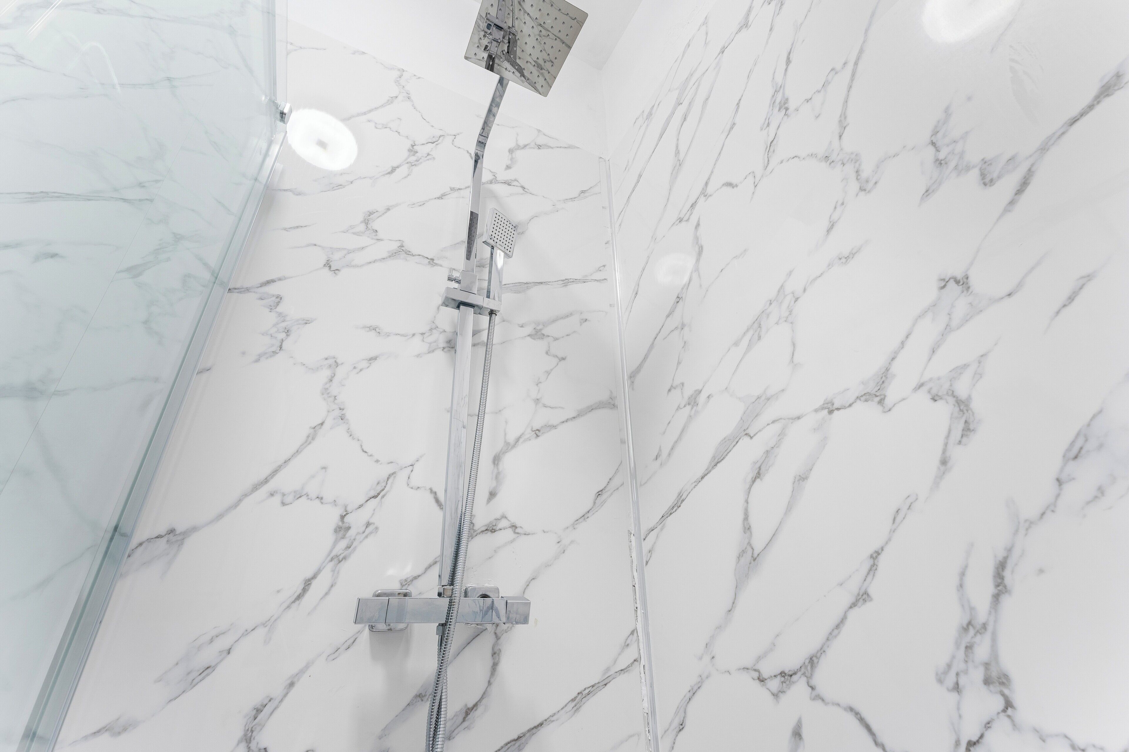 Une douche équipée d’un pommeau de douche à main fixé au mur, le mur étant recouvert d’un motif imitant le marbre.