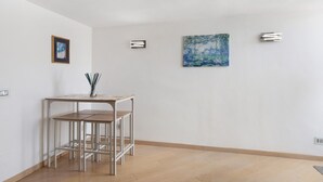 Ein Zimmer mit Holzboden, einem Metalltisch mit Stühlen, einem gerahmten Bild und zwei Wandleuchten.