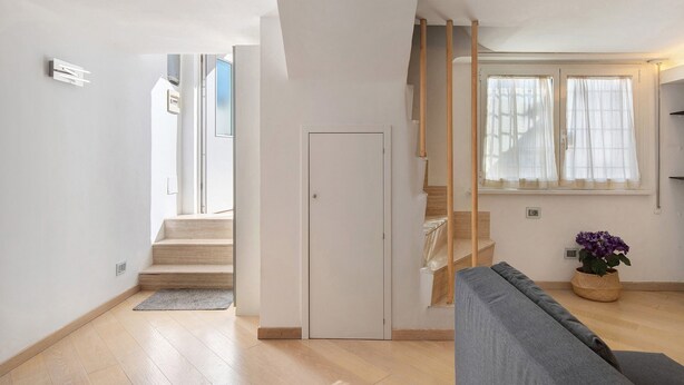 Ein modernes Interieur mit einer Treppe, einem grauen Sofa und einem Blumentopf.