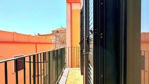 Ein schmaler Balkon mit Metallgeländer, Fliesenboden und Blick auf benachbarte Gebäude.