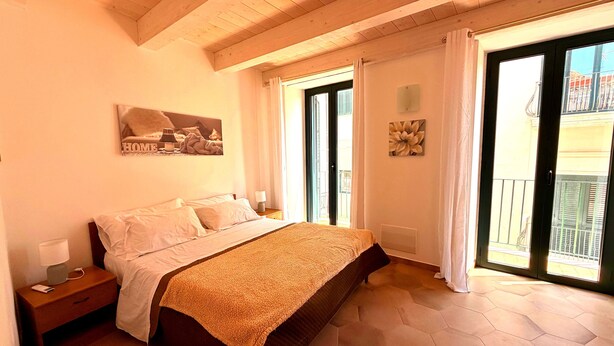Ein Schlafzimmer mit Bett, Nachttisch, Fenster mit Vorhängen und Blick nach draußen.