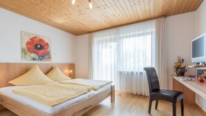 Ein Schlafzimmer mit einem hölzernen Bett, einem Schreibtisch mit Computer, einem Stuhl und einem Fenster mit Vorhängen.