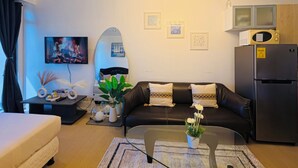 Un soggiorno moderno con un divano, un tavolino in vetro, una TV a schermo piatto, un forno a microonde e un frigorifero.
