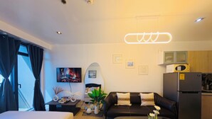 Una moderna camera d'albergo con un letto, una poltrona, un tavolo da pranzo, una TV, un forno a microonde e un frigorifero.