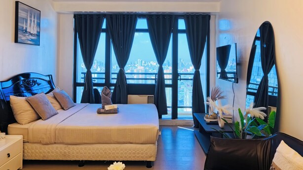 Una moderna camera d'albergo con un letto grande, una scrivania, una sedia, una televisione e vista sulla città attraverso ampie finestre.
