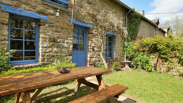 Ein Steinhaus mit blauen Fensterrahmen und einem Holztisch im Garten.