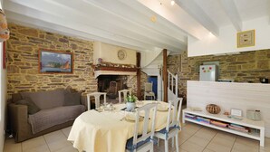 Una habitación acogedora con pared de piedra, chimenea, una mesa de comedor preparada para cuatro personas, un sofá y una estantería.