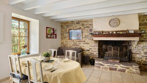 Un comedor con chimenea de piedra, un reloj y una ventana con vistas a árboles.