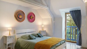 Un dormitorio con una cama, dos lámparas de noche, un ventanal con cortinas y dos adornos de pared.