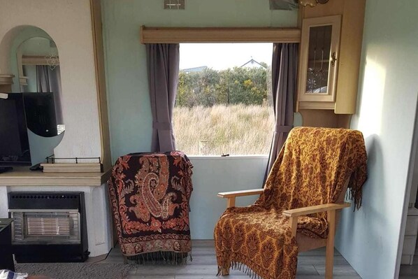 Una habitación con una silla de madera cubierta con una manta estampada, un televisor y una ventana con cortinas.