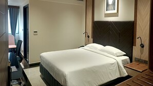 A modern hotel room with a large bed, a ceiling fan, a bedside table, and a wall-mounted artwork. - Crystal Residency (Tiruchirappalli)