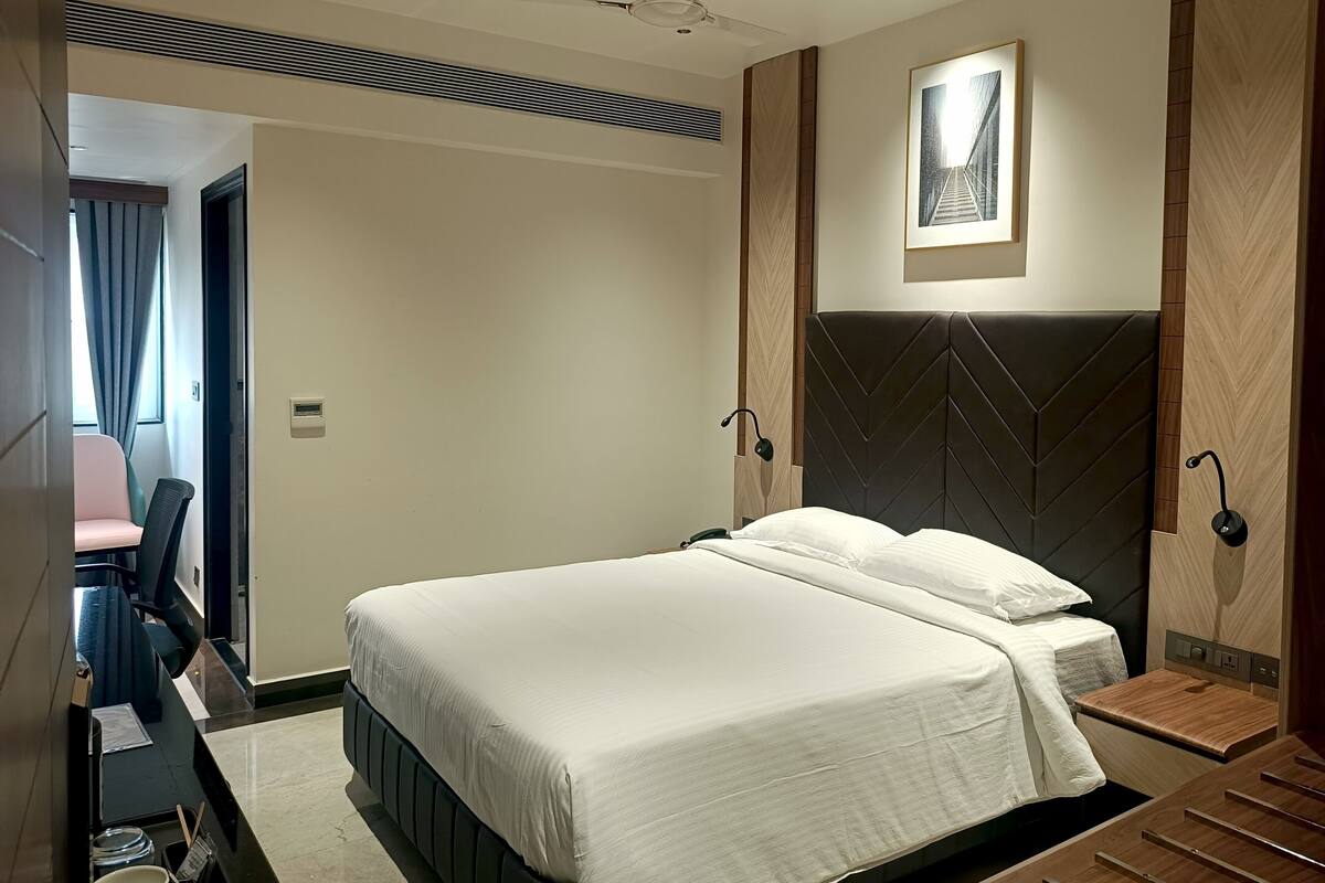 Moderni hotellihuone, jossa on suuri sänky, kattotuuletin, yöpöytä ja seinälle kiinnitetty taideteos.