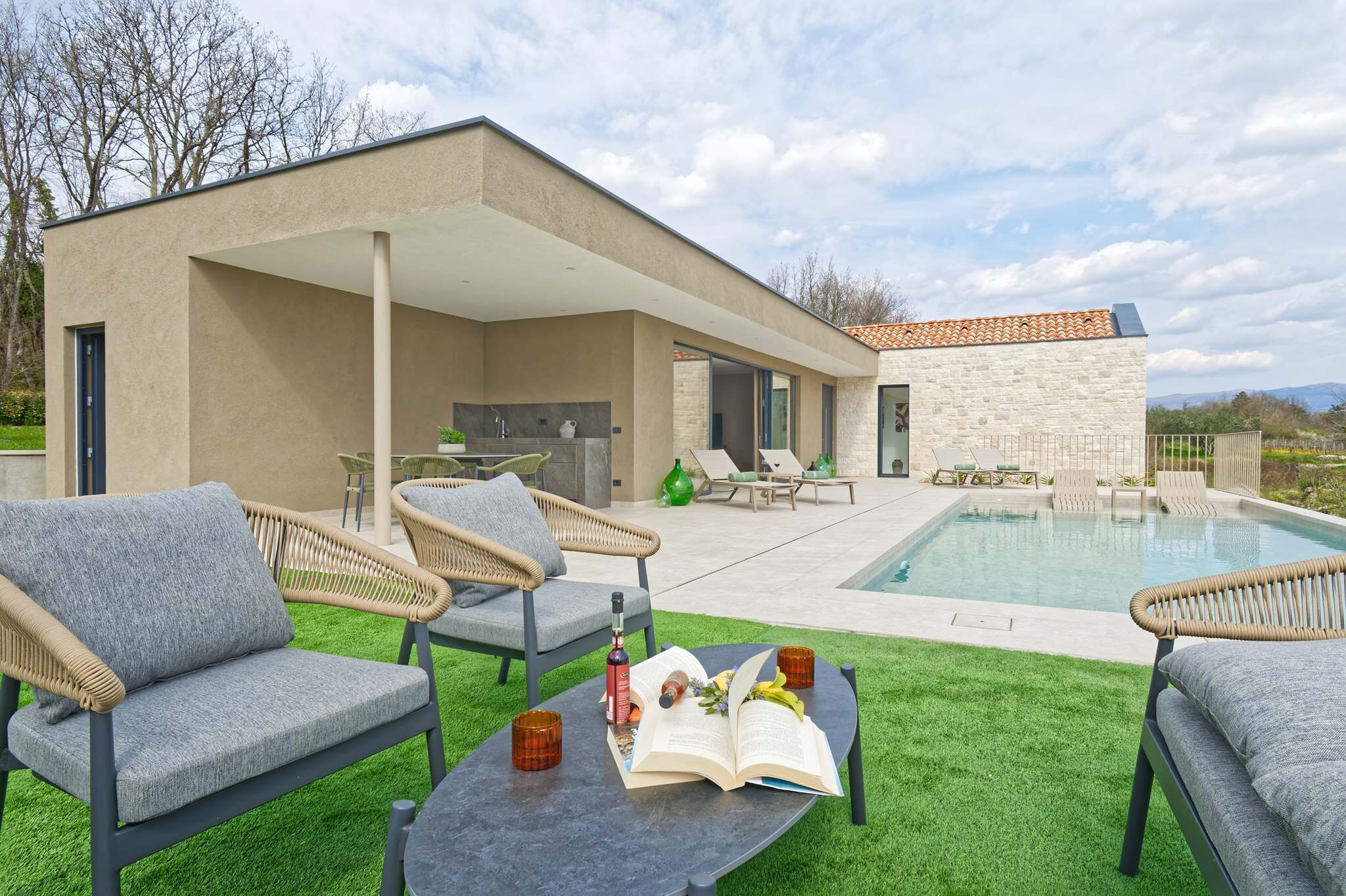 Una casa moderna con piscina, mobiliario exterior y un porche cubierto.