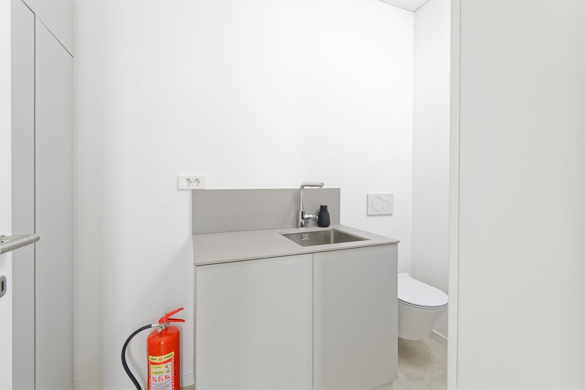 A small, modern bathroom with a sink, toilet, and a fire extinguisher.