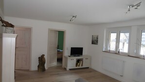 Ein großzügiger Wohnbereich mit Fernseher auf einer weißen Kommode, einem grauen Sofa und einem Esstisch.