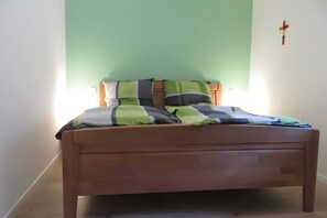 Una cama individual con estructura de madera, colcha a rayas verde y gris, y almohada blanca.