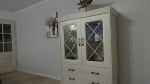 Ein weißes Schränkchen mit Glastüren und Schubladen, eine Holzskulptur darauf und ein gerahmtes Bild an der Wand.