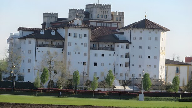Ein großes, mehrgeschossiges Gebäude mit einer schlossartigen Fassade, das mehrere Balkone und eine Flagge auf dem Dach hat.