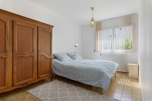 Une chambre à coucher comprenant un lit, une armoire en bois, un radiateur, une fenêtre et un luminaire suspendu.