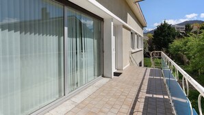 A building with large sliding glass doors, a tiled balcony, and a view of mountains in the background. - Apartment 'Maison Grenoblois' with Balcony (Eybens)