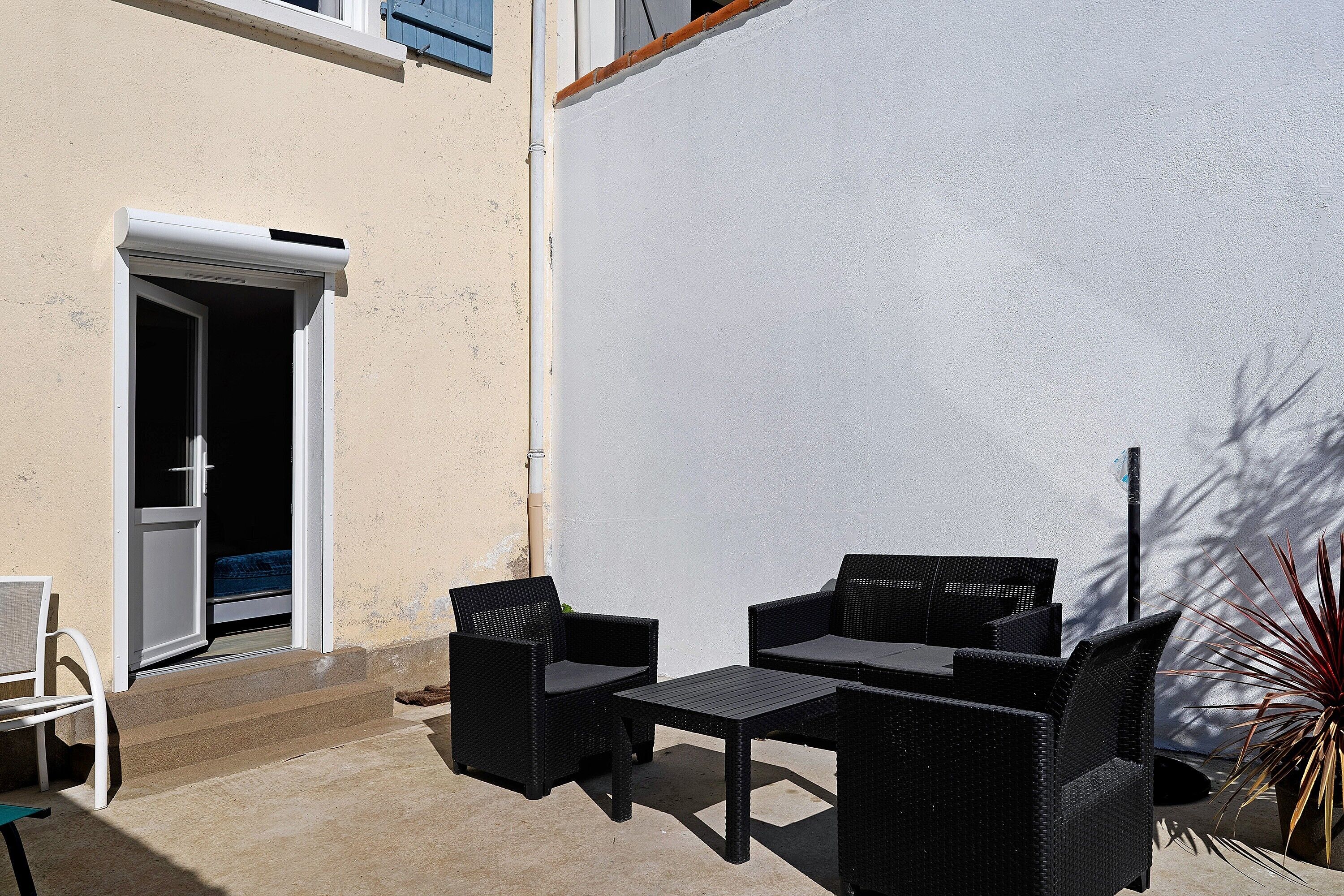 An outdoor patio with wicker furniture, a door, and a plant.