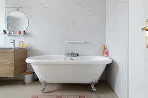A bathroom with a freestanding bathtub, a wooden vanity, a mirror, and a marble-patterned wall.