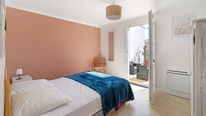 Un dormitorio con cama, una silla, una puerta y un ventanal.