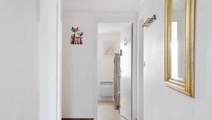 Un pasillo con pared blanca, un espejo con marco dorado y una puerta que da a otra habitación.