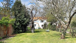 Una propiedad residencial con césped cuidado, árboles maduros y un edificio blanco de techo rojo.