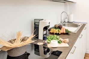 Eine Küche mit modernem Design, inklusive einer Spüle aus Edelstahl, einer integrierten Kaffeemaschine und einer Auswahl frischer Gemüsesorten auf der Arbeitsfläche.