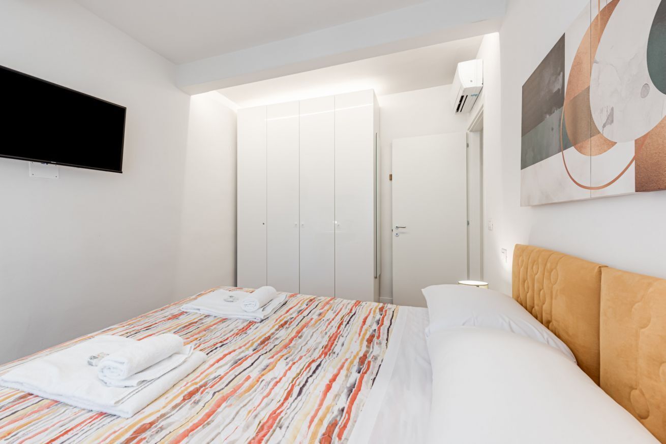 Una habitación de hotel con una cama, un televisor de pantalla plana montado en la pared, un armario y un cuadro en la pared.