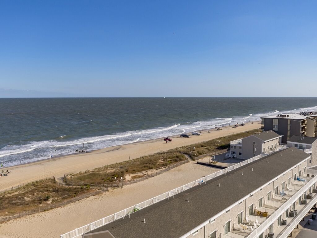 Un hotel frente al mar con vista a la playa, estacionamiento y una larga edificación con varios balcones.