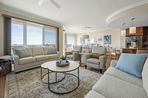 Ein geräumiges Wohnzimmer mit großem Fenster, einer Couch, einem Couchtisch und einem Essbereich mit Stühlen und Tisch.