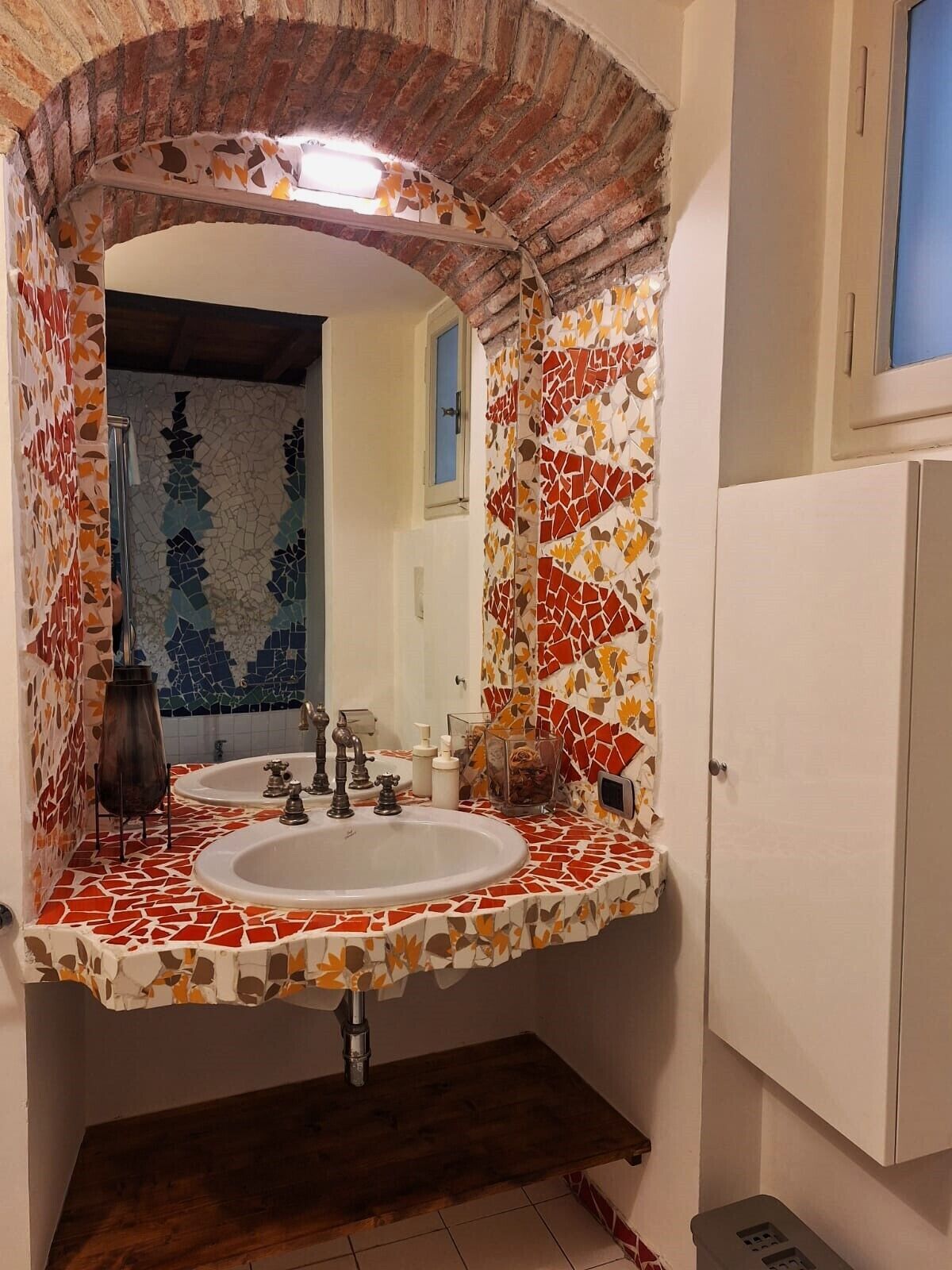 Um banheiro com pia em mosaico, espelho e um banco de madeira.