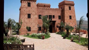 A large, traditional building with a central entrance, surrounded by a garden with palm trees and flowering plants. - kasbah illy (Tifni)