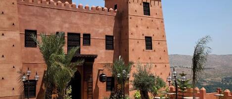 Un edificio tradicional marroquí con patio, palmeras y montañas al fondo.