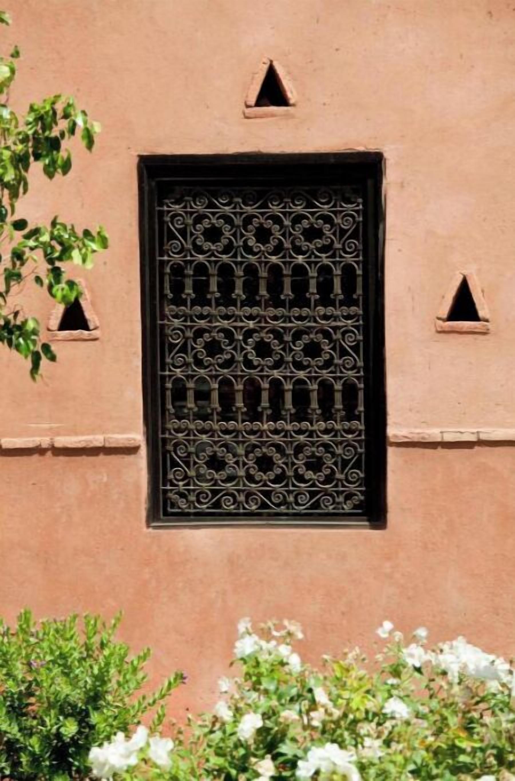 Fachada de edificio con un ventanal decorativo, pequeñas ventanas triangulares y una pared texturizada.