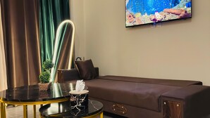 Moderni olohuone, jossa on ruskea sohva, musta ja kultainen sohvapöytä, seinälle asennettu televisio ja ruukussa oleva kasvi.