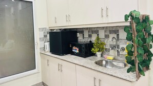 Keittiössä on valkoiset kaapit, musta mikroaaltouuni, pesuallas ja ikkuna, jossa on himmeälasinen ovi.