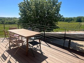 Una terraza de madera con mesa y sillas, con vistas a un viñedo.