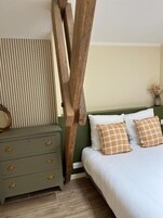 Un dormitorio con una cama, un aparador, una escalera de madera y una pared a rayas.