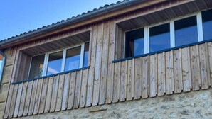Un bâtiment avec un revêtement en bois et des murs en pierre, doté de deux fenêtres à cadres blancs et d’un petit balcon.